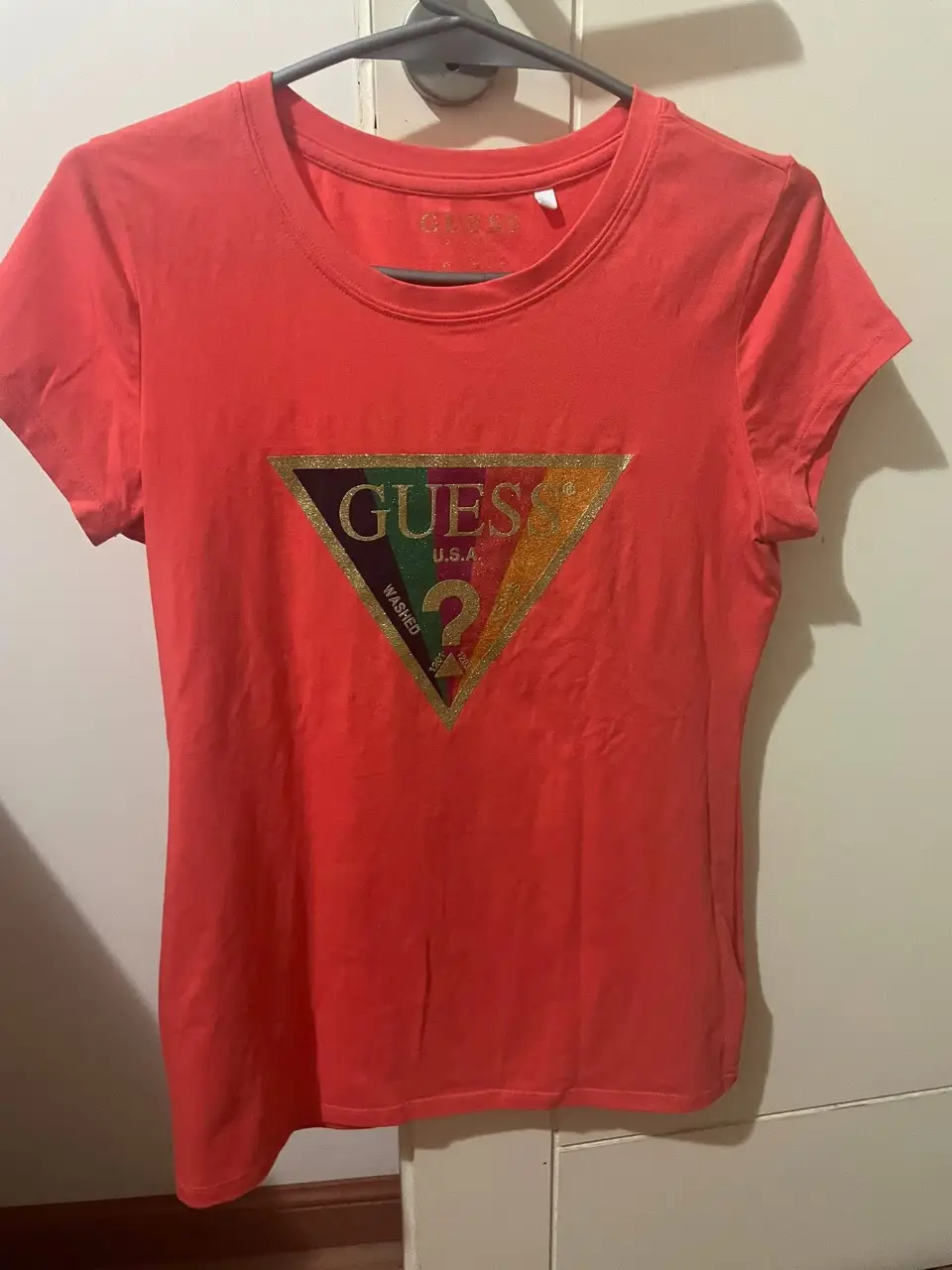 Remera Guess de mujer, color naranja coral con logo triangular Guess estampado en el frente. Ideal para un look casual y moderno.