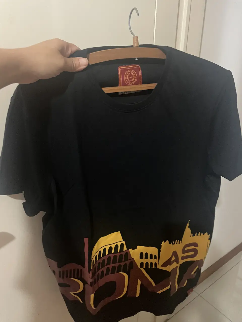 Remera negra de AS Roma con estampado del escudo y la silueta de la ciudad en amarillo y borgoña. Ideal para fanáticos del fútbol.