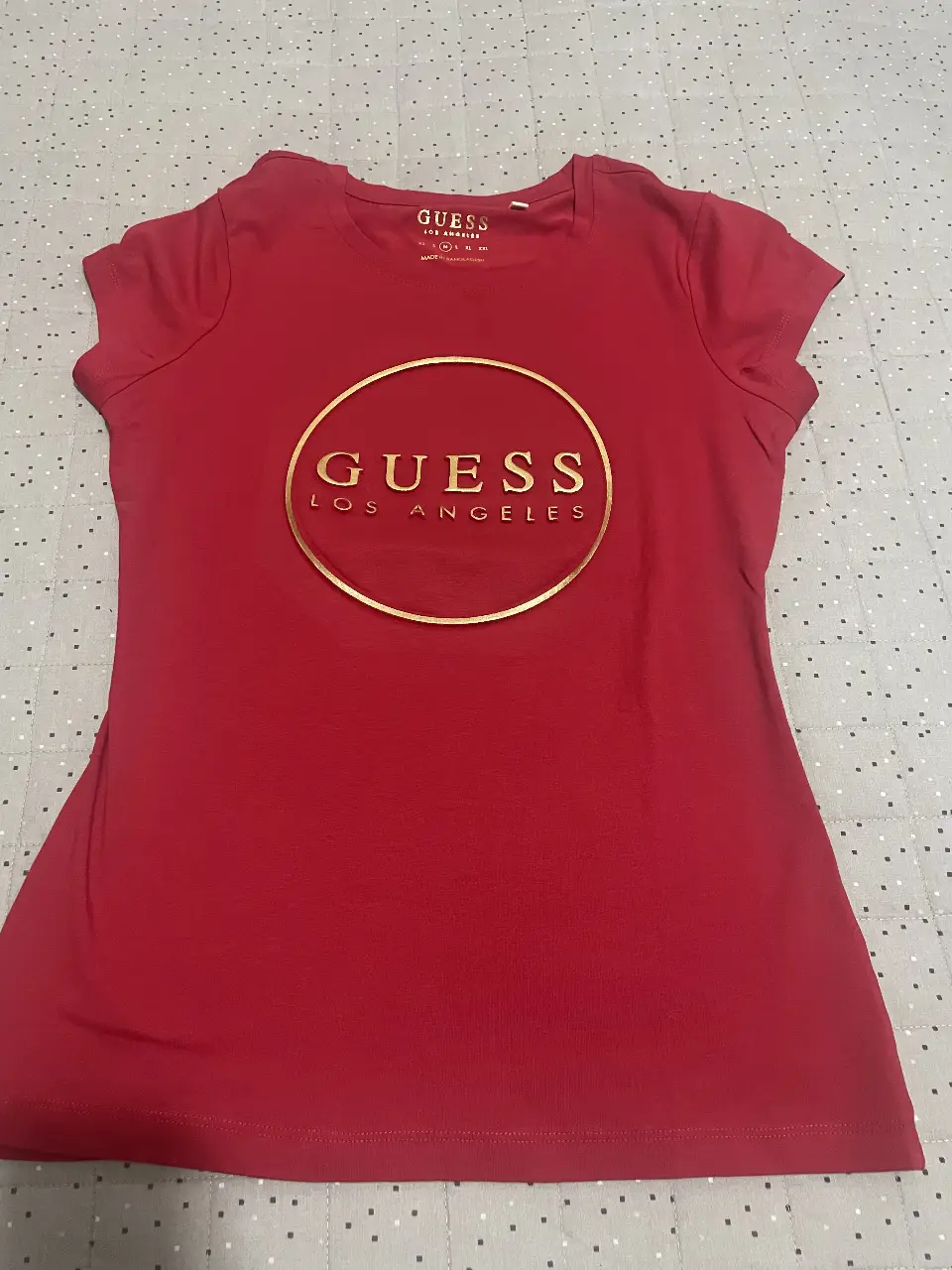 Remera Guess roja con logo dorado en el frente. Ideal para un look casual y moderno.