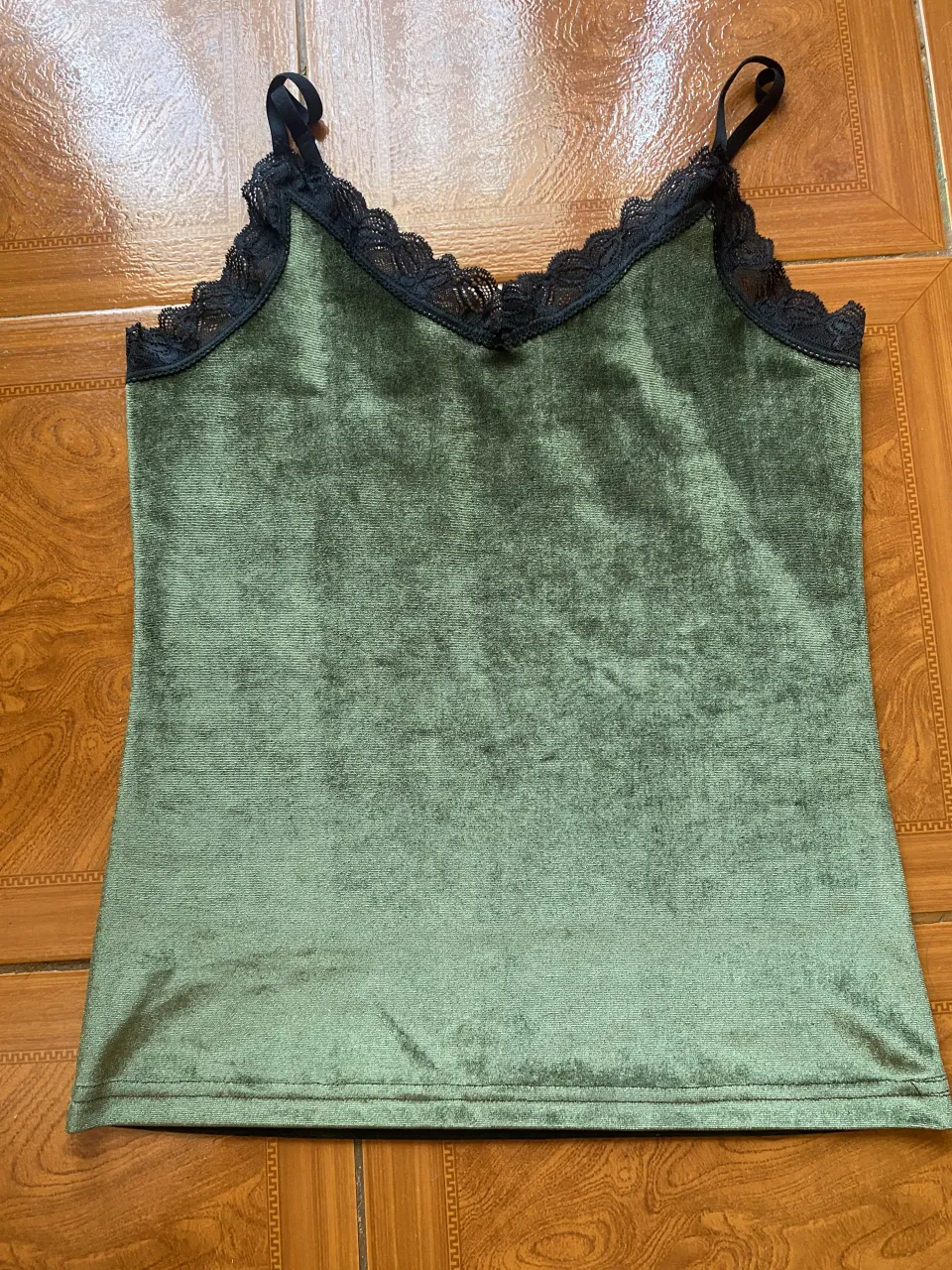 Musculosa verde con detalles de encaje negro en el escote y breteles finos. Espalda con breteles regulables.
El color no se distingue por la tela y la luz pero es un verde oscuro mas bien bosque? 