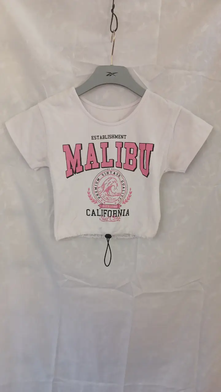 Remera crop top blanca con estampado "Malibu" en rosa. Ideal para un look casual y playero.