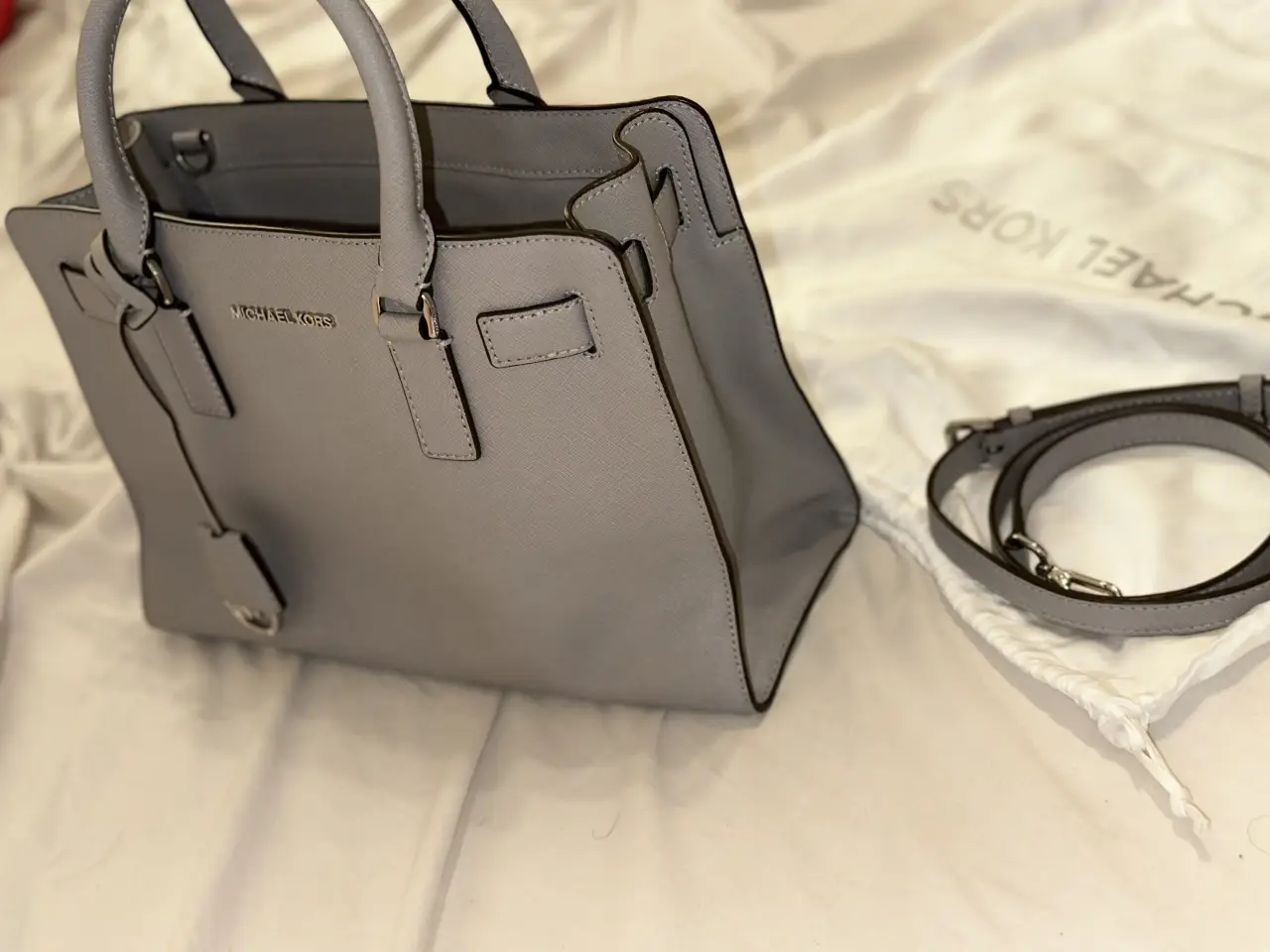 Cartera Michael Kors modelo Satchel en color gris claro. Confeccionada en cuero sintético, incluye correa para llevar al hombro y bolsa protectora.