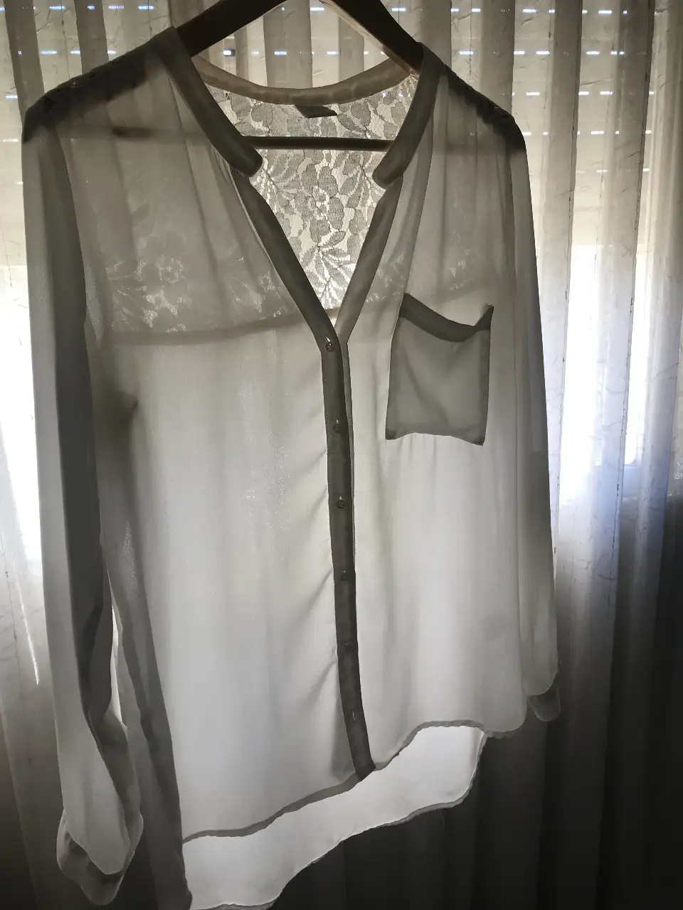 Blusa blanca con detalle de encaje en el frente y espalda. Tiene un bolsillo en el pecho y botones en la parte delantera. Ideal para un look elegante y femenino.
