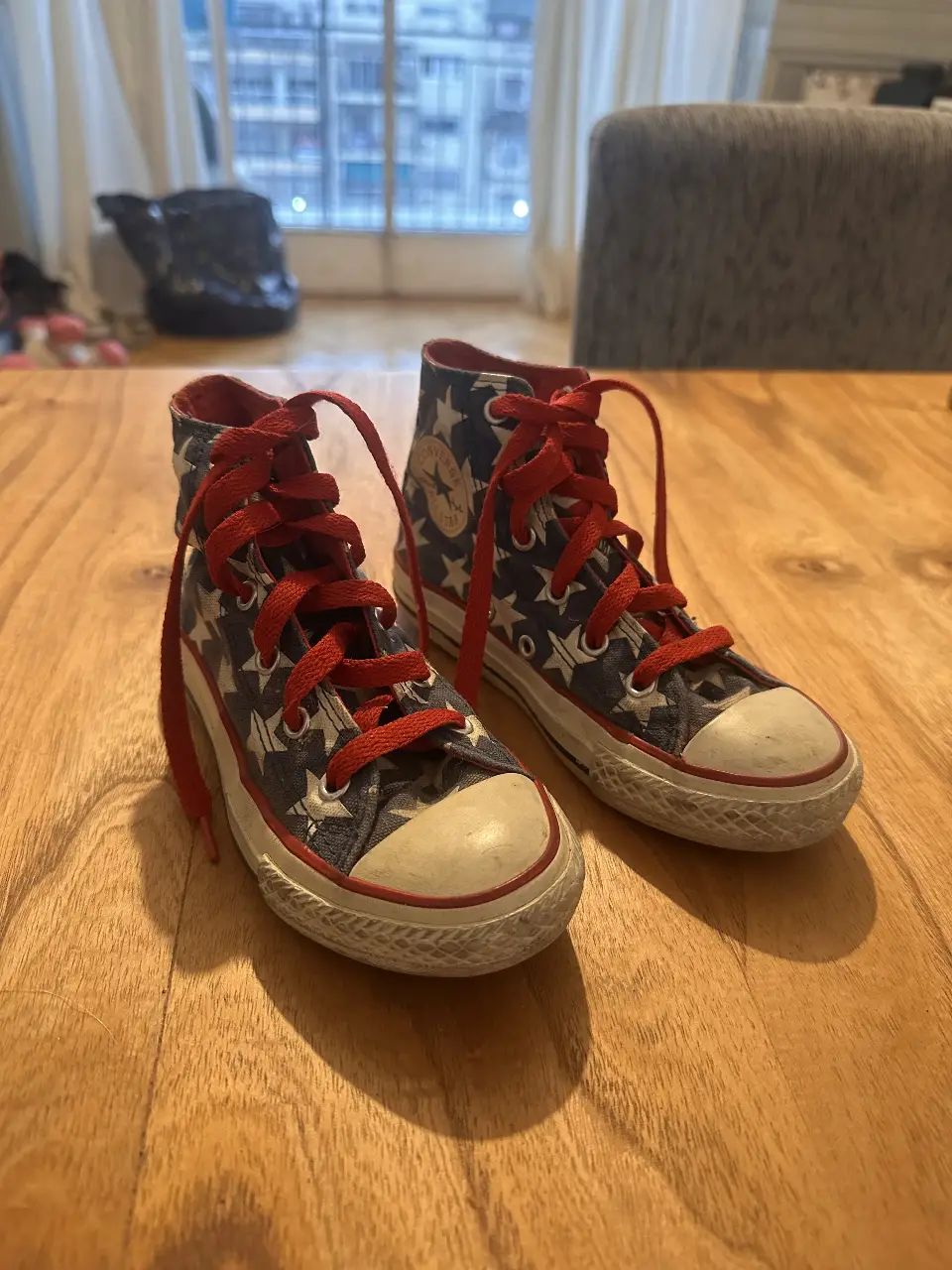 Zapatillas Converse All Star de caña alta con diseño de estrellas y bandera americana. Cordones rojos y suela de goma.