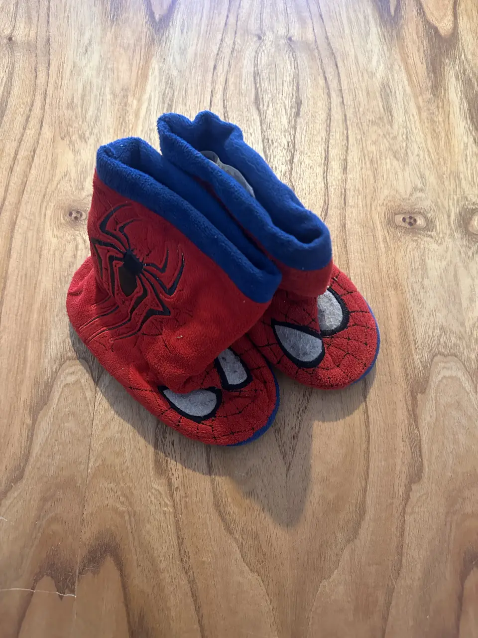 Pantuflas de Spiderman para niños, rojas con detalles azules y la cara de Spiderman en la parte delantera. Ideales para mantener los pies abrigados y cómodos en casa.