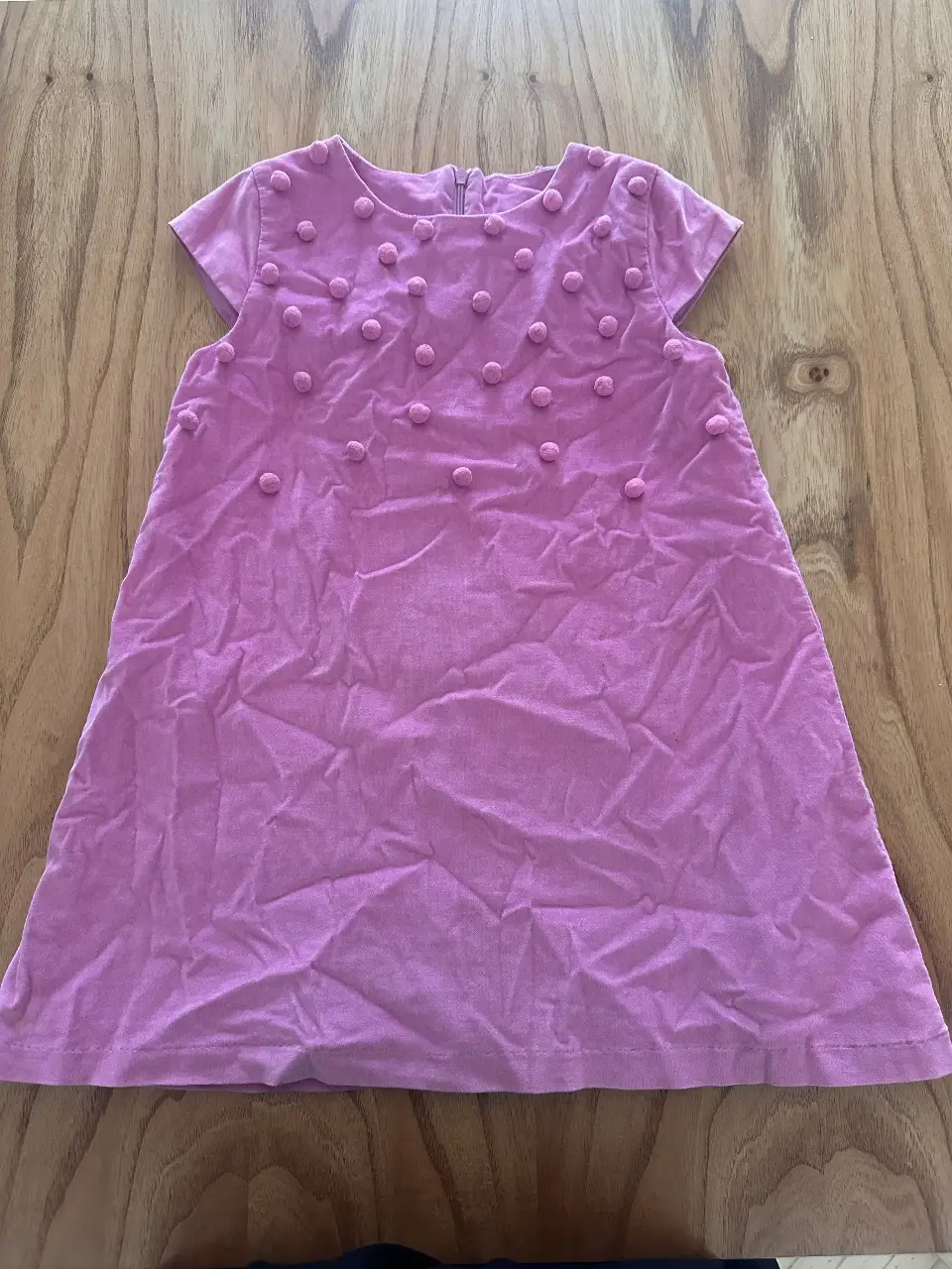 Vestido mini rosa con detalles de pompones en la parte superior. Ideal para ocasiones especiales o para un look casual con un toque de originalidad.