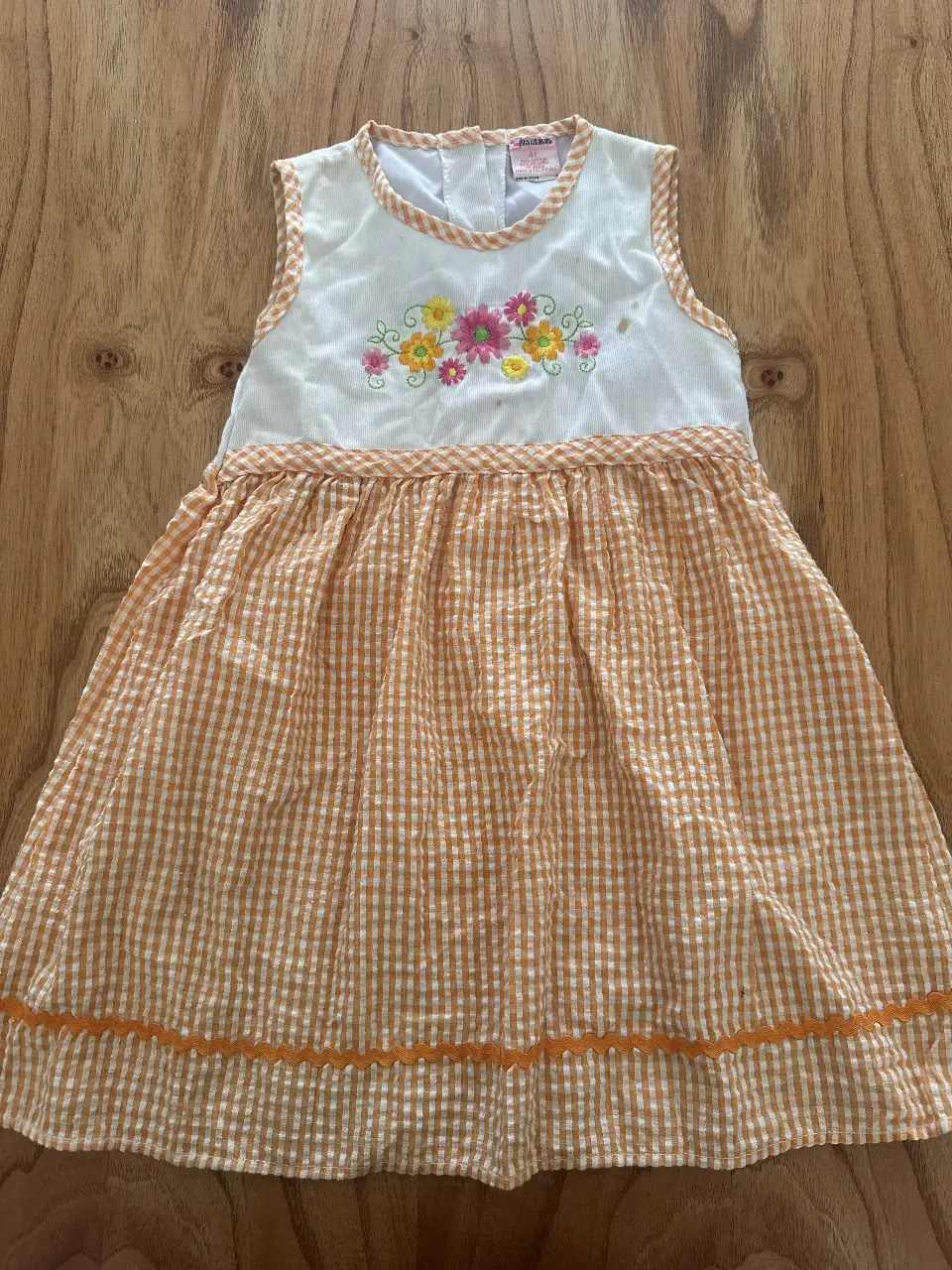 Vestido de niña, sin mangas, con estampado floral en la parte superior y falda a cuadros naranja y blanca. Ideal para el verano.