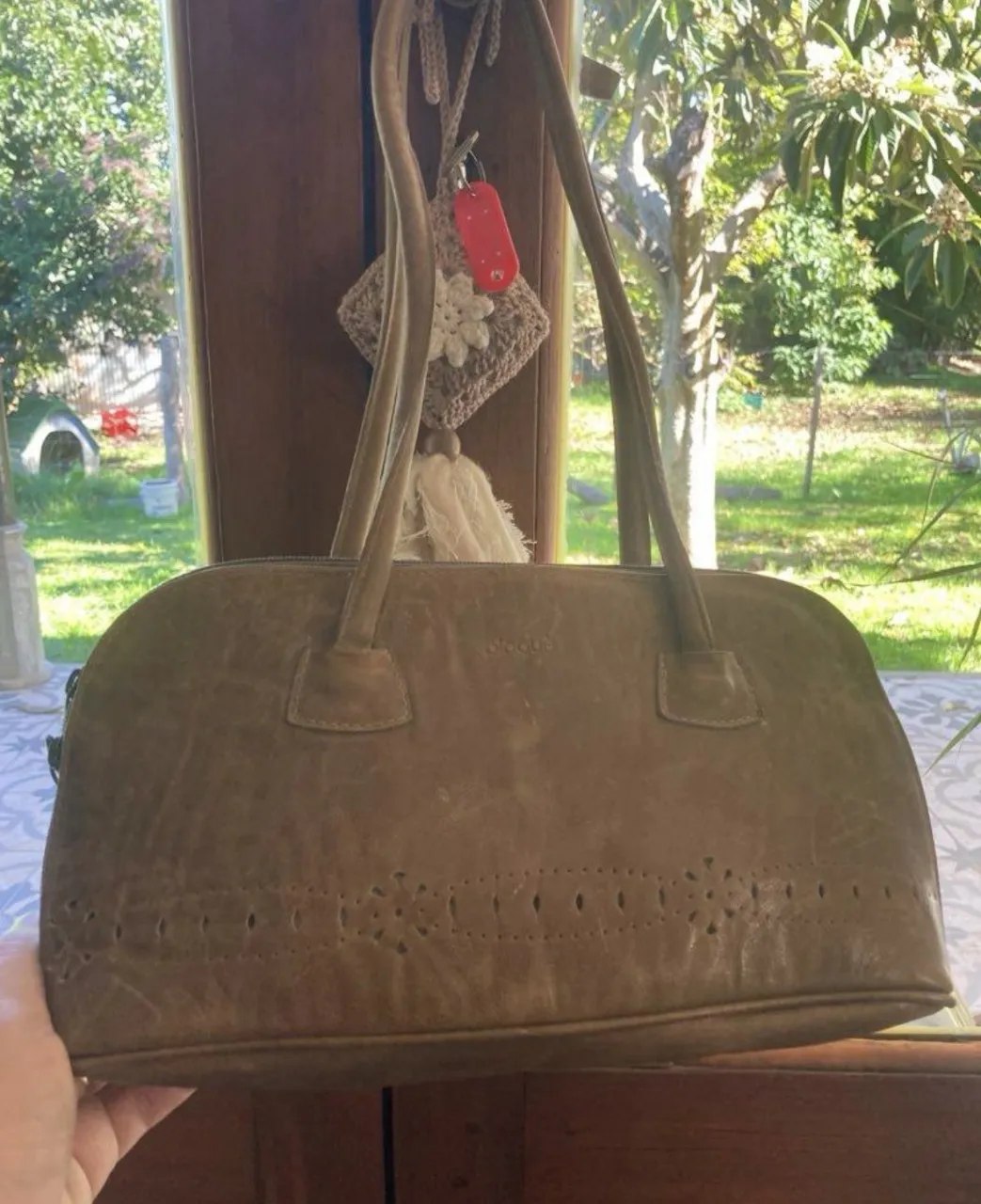 Bolso de cuero color suela con detalles de perforaciones en la parte inferior. Tiene dos asas cortas y un cierre superior.