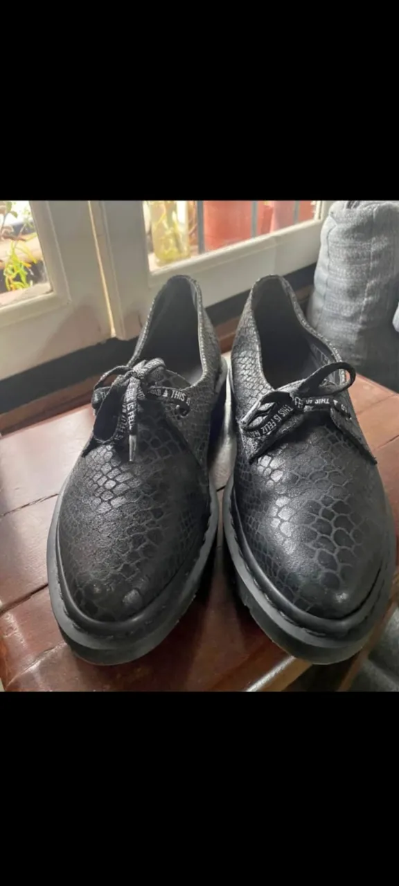 Zapatos Dr. Martens negros con diseño de piel de serpiente. Cordones con la marca. Suela resistente y cómoda, ideales para un look moderno y urbano.