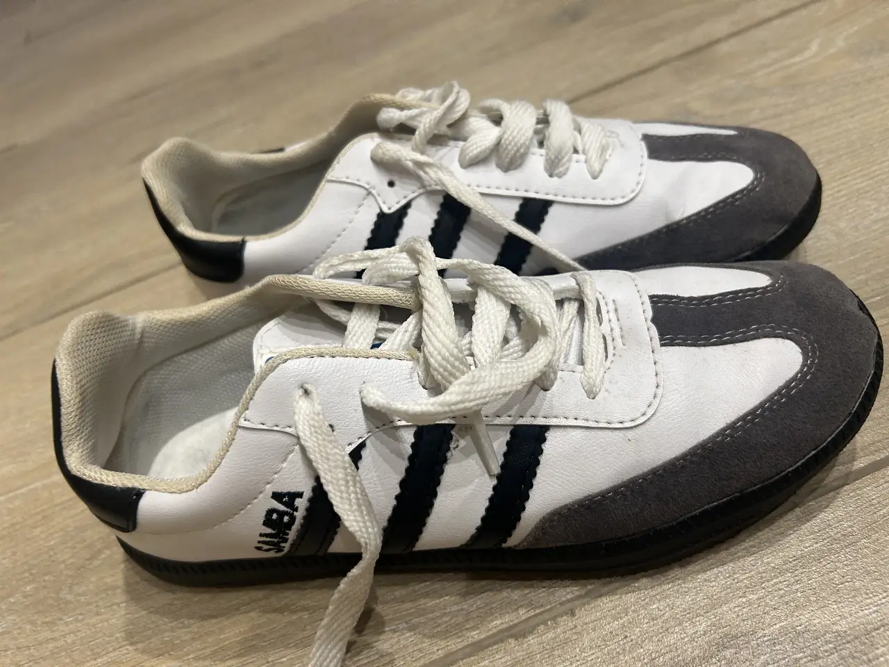 Zapatillas Adidas Samba blancas con detalles en negro y gris. Diseño clásico y atemporal, ideales para un look casual y urbano.