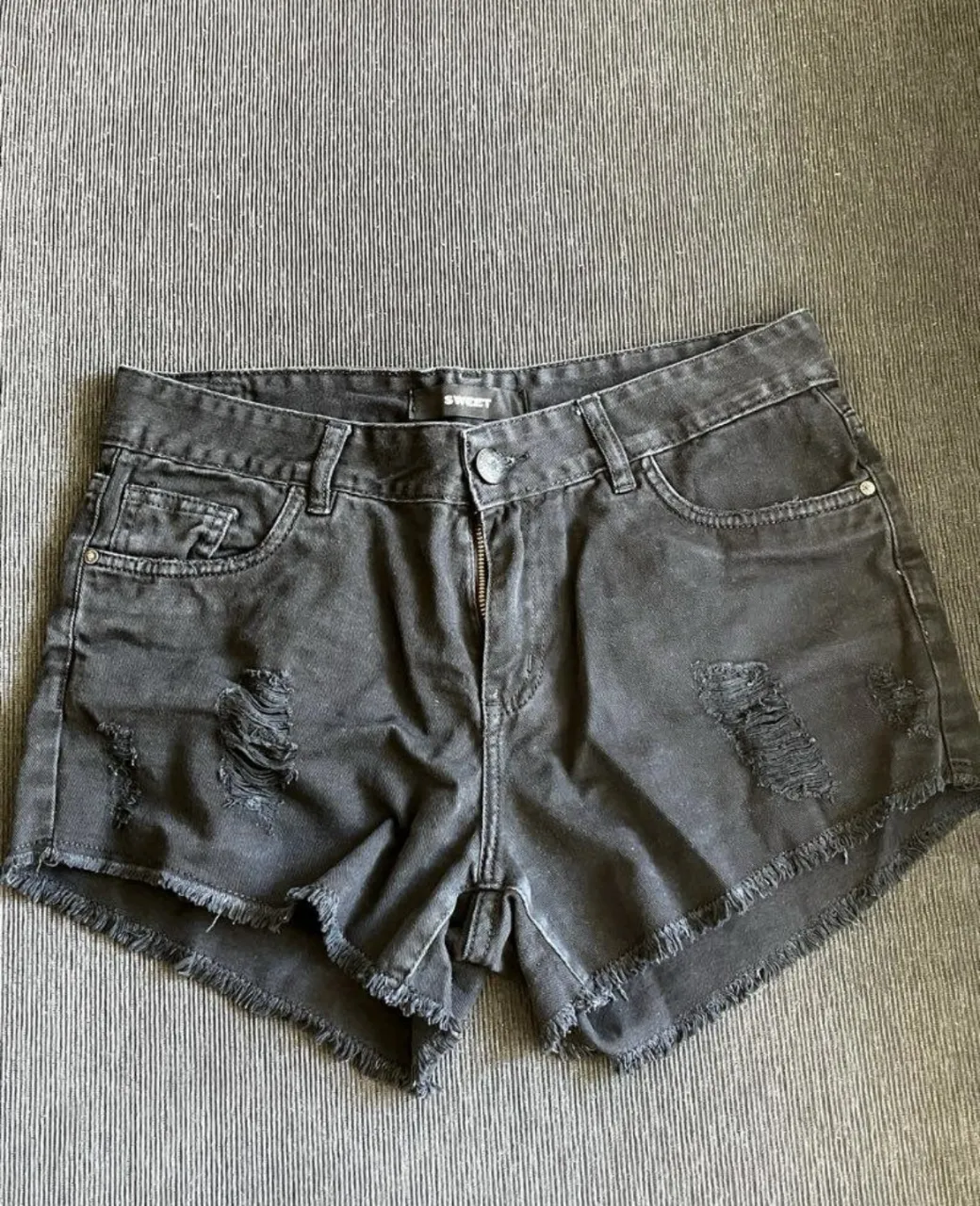 Short de jean negro con roturas y flecos en el borde. 