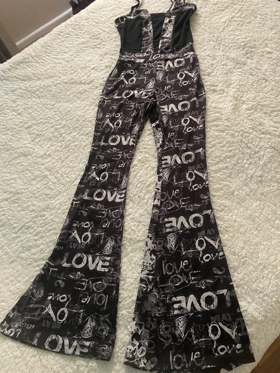 Mono largo con estampado de la palabra LOVE en blanco sobre fondo negro. Tiene tirantes finos y un diseño de pantalón acampanado.
