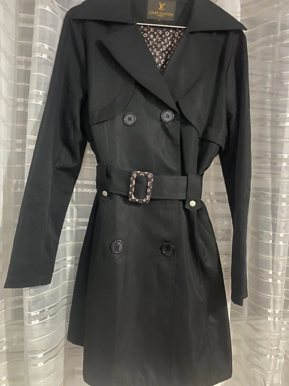 Trench coat negro de mujer, con cinturón y hebilla con monograma. Ideal para un look elegante y sofisticado.