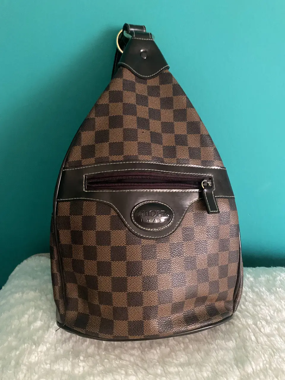 Bandolera marrón con diseño de cuadros, ideal para llevar tus esenciales con estilo. Cuenta con un bolsillo frontal con cierre y una correa ajustable para mayor comodidad. Perfecta para un look casual y moderno.
