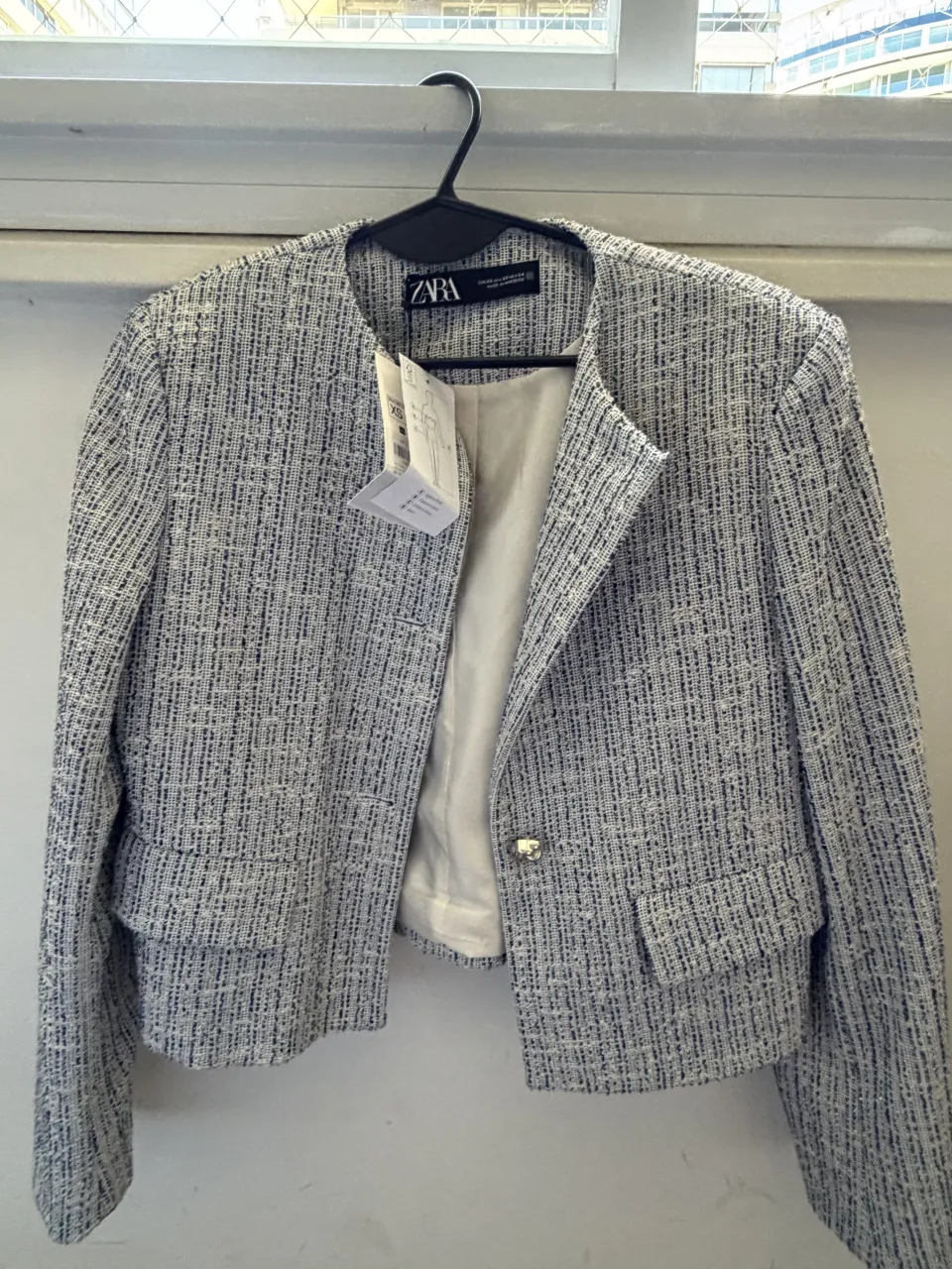 Blazer corto de tejido texturizado con cuello mao y un botón metálico al frente. Posee dos bolsillos con solapa en la parte inferior.