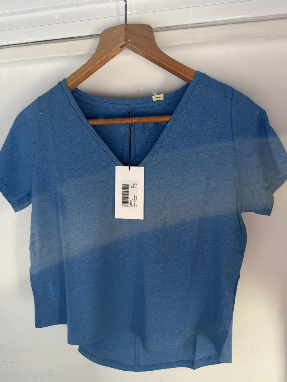 Remera azul de escote en V y mangas cortas. Posee una etiqueta colgante blanca con código de barras y detalles del producto.