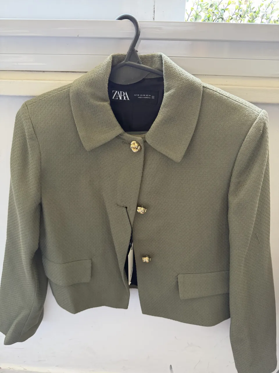 Blazer corto de color verde. Tiene botones dorados y bolsillos frontales.