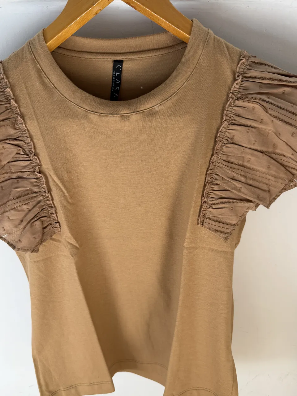 Remera de manga corta color tiza con detalles de volados y tela de red en las mangas. Cuello redondo.