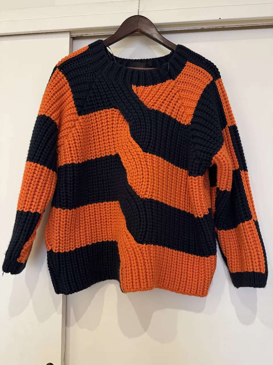 Sweater de punto grueso con diseño geométrico en bloques naranja y azul marino. Cuello redondo y mangas largas. Ideal para un look casual y abrigado.