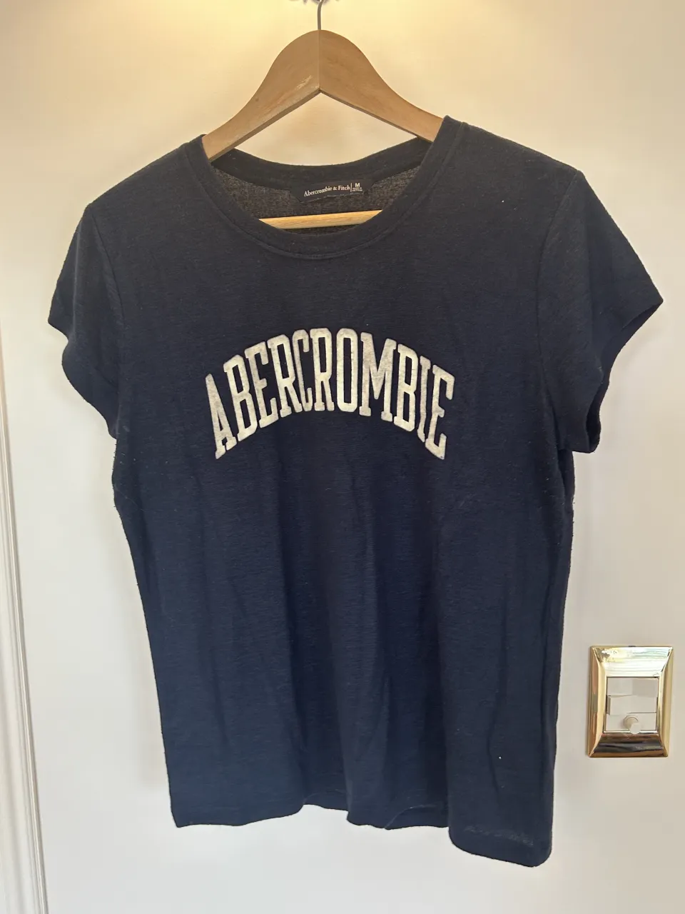 Remera azul marino con estampa blanca "Abercrombie" en el frente.