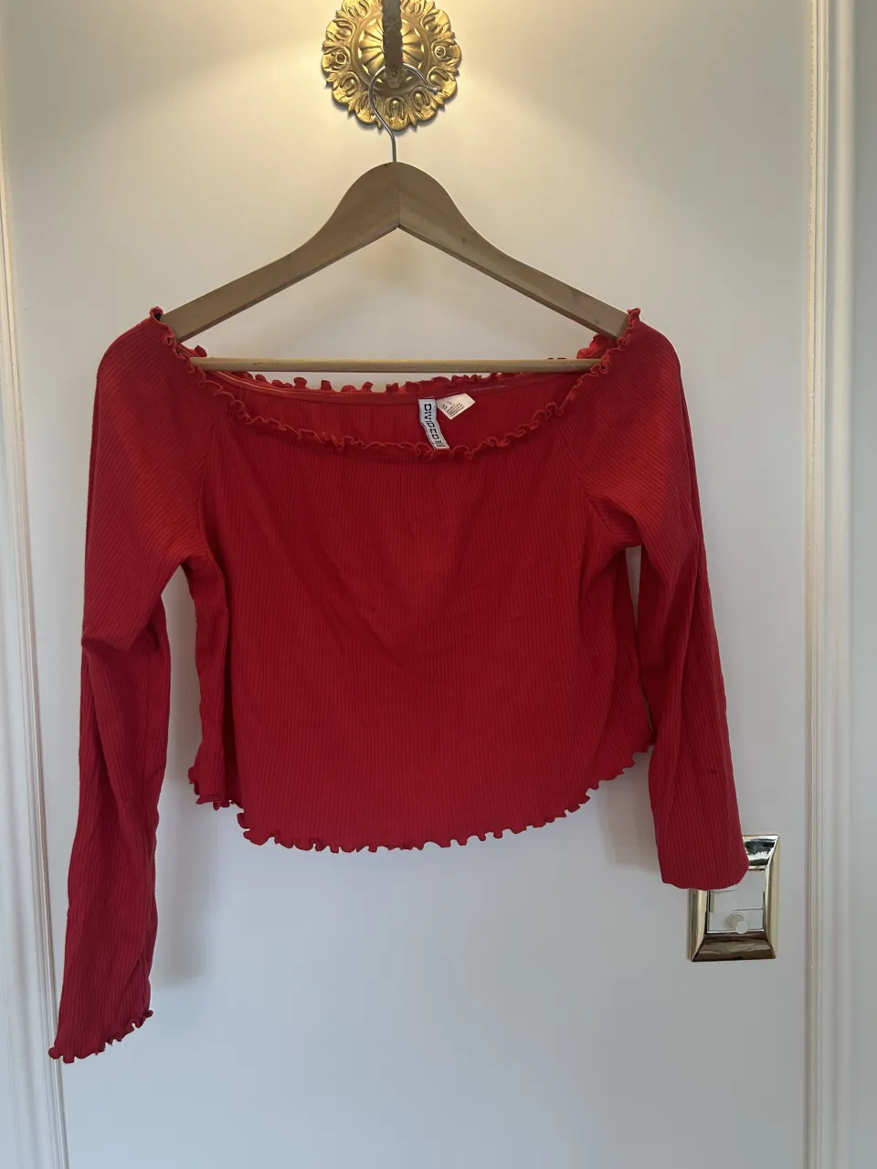 Remera roja escote bote, con mangas largas y volados en cuello y ruedo.