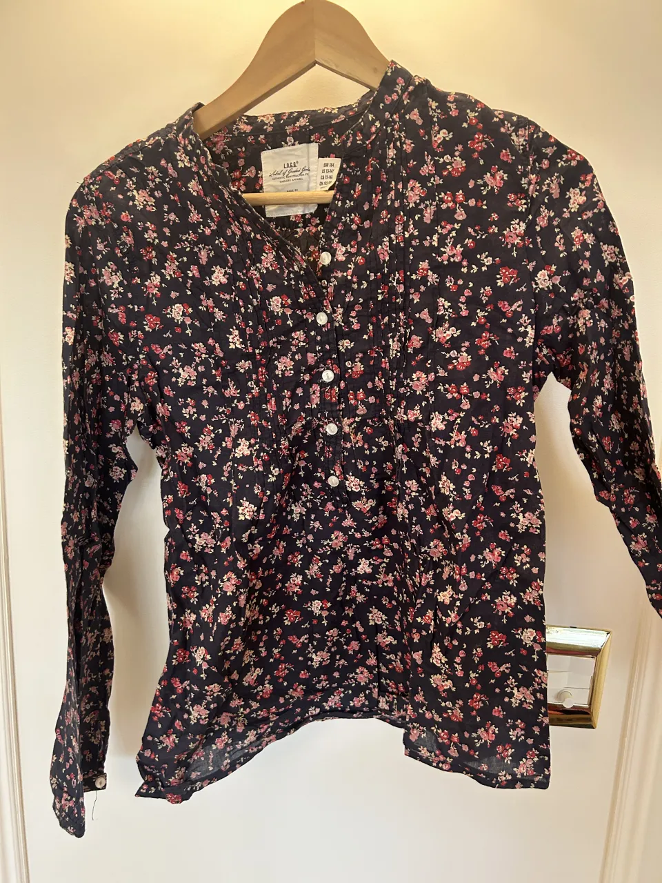 Camisa estampada con flores pequeñas en tonos rosas y rojas sobre fondo azul oscuro. Posee cuello mao y botones al frente.