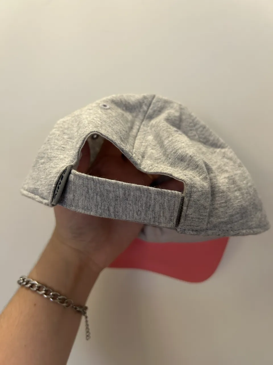 Gorra de tela gris con visera rosa. Posee etiqueta interior con detalles de la marca.