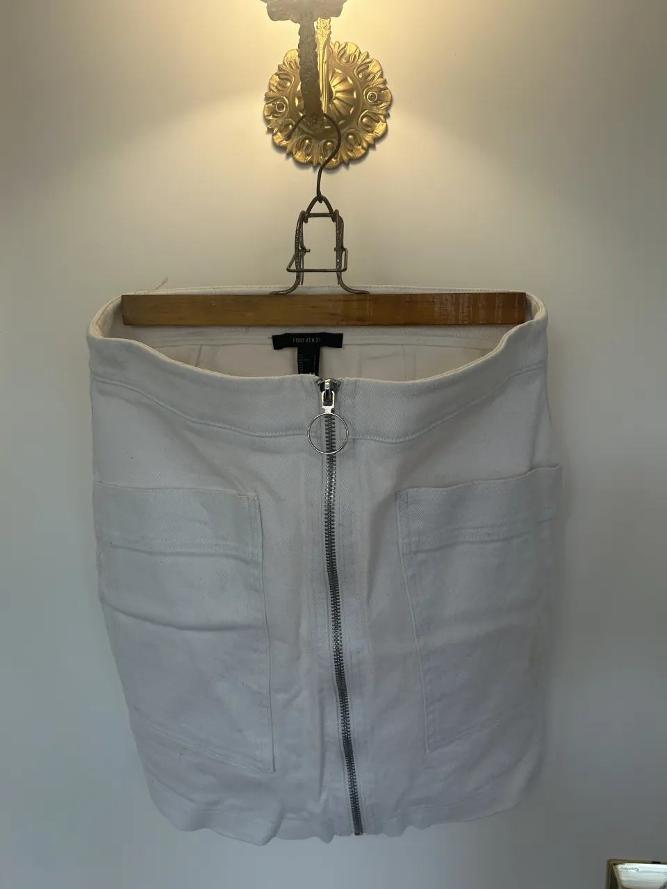 Pollera blanca de jean con cierre metálico al frente y bolsillos. Tiene una Manchita amarilla en el bolsillo delantero derecho (se ve en la 3er foto)