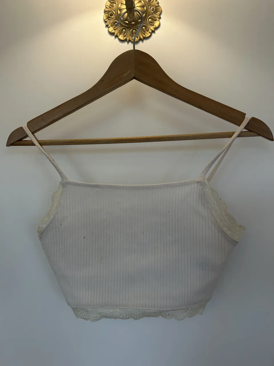 Top blanco de breteles finos con detalles de encaje en el borde inferior y en la parte superior del busto. Posee un cierre en la espalda.