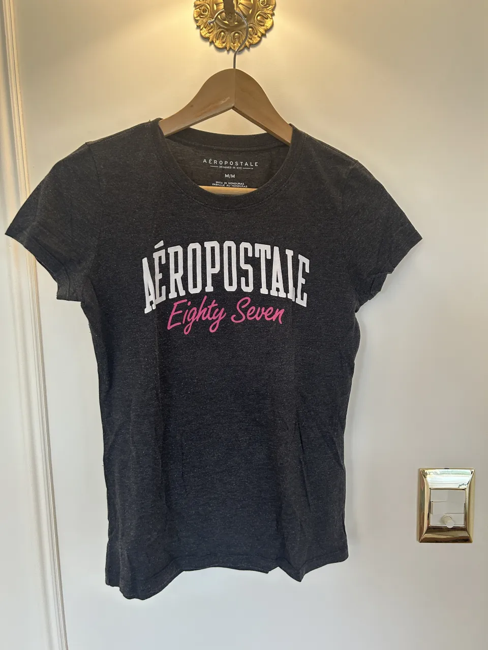 Remera gris oscuro con estampa blanca y rosa que dice "AEROPOSTALE Eighty Seven".