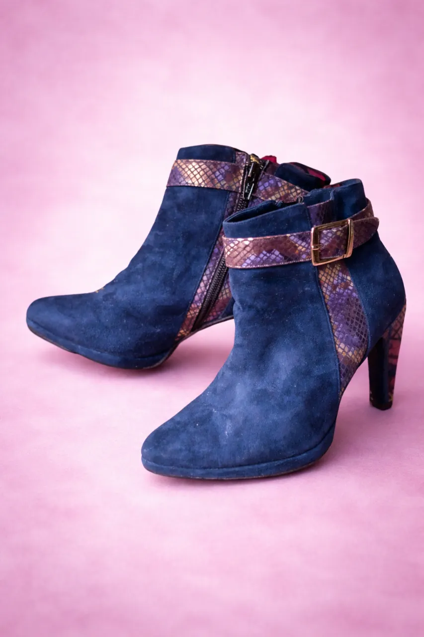 Botitas de gamuza azul marino con detalles de serpiente en tonos morados y dorados. Tienen una hebilla y cierre lateral para un ajuste perfecto. Ideales para darle un toque chic a tus looks de otoño o invierno.