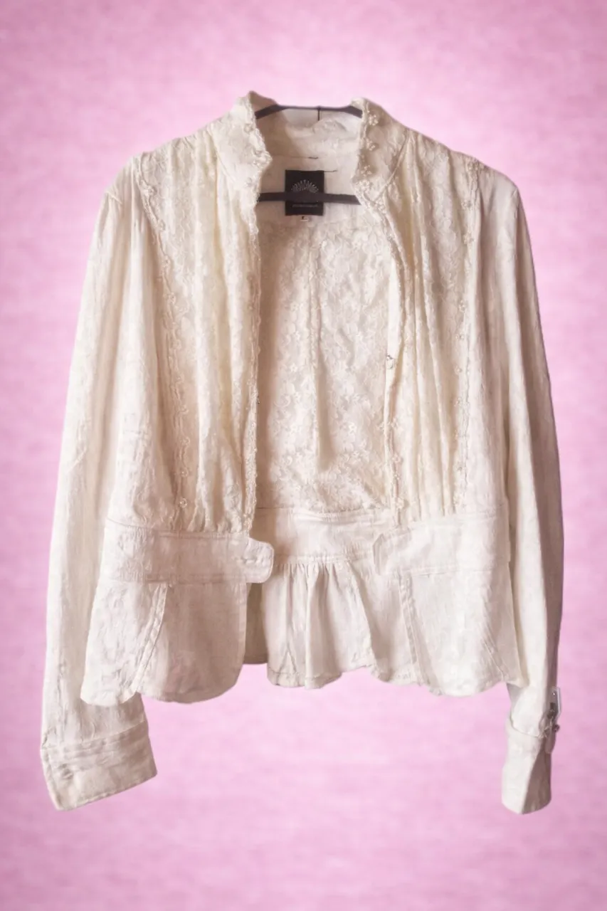 Campera blanca de Brocato y encaje con cuello mao y volado en la cintura. Posee botones al frente y detalles de bordado floral.