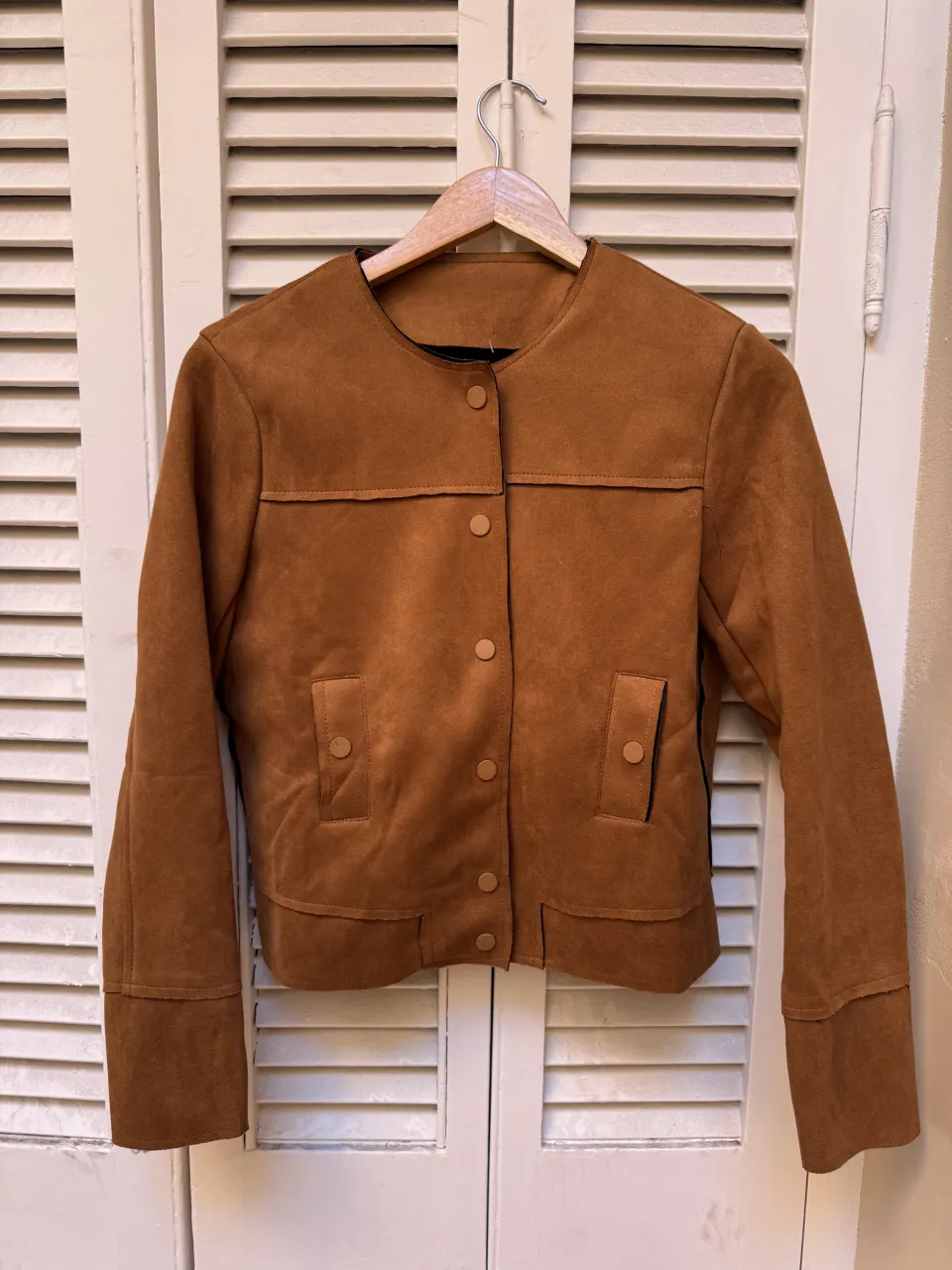 Campera de gamuza marrón, súper canchera y versátil. Tiene botones al tono y bolsillos frontales. Ideal para darle un toque chic a cualquier look. 