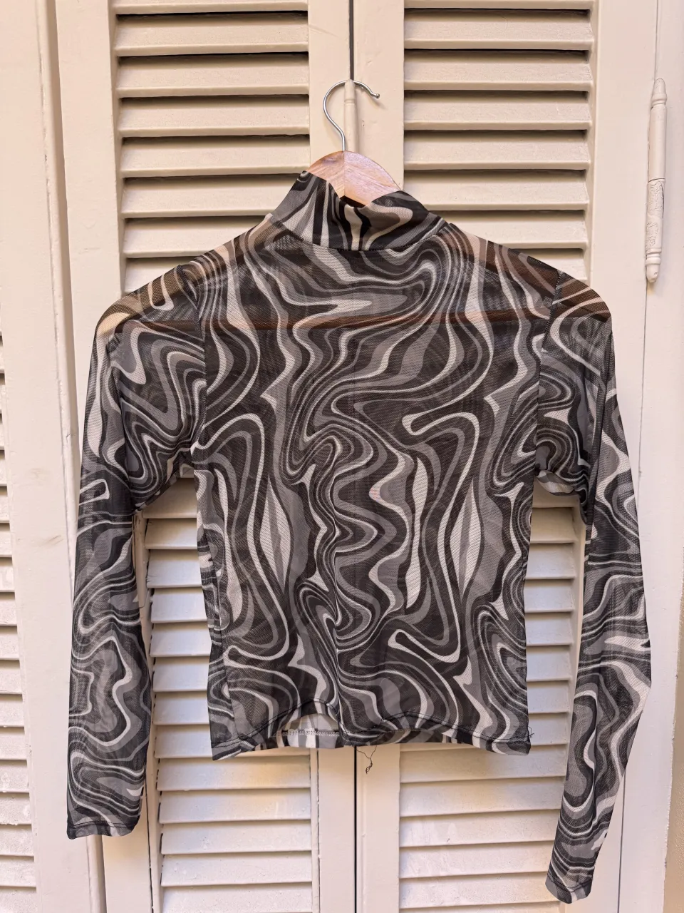 top de microtul con mangas largas,  cuello alto y estampa psicodélica en tonos grises, negros. Transparente, ideal para un look audaz y moderno.