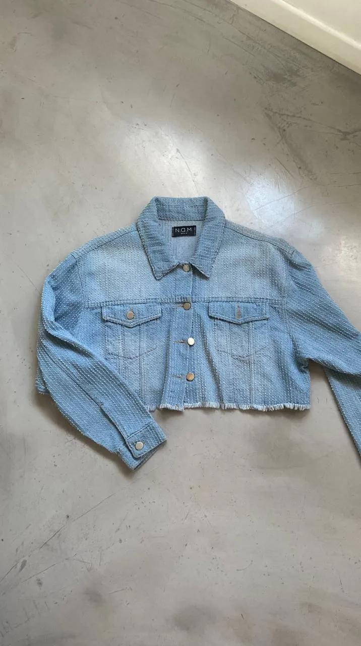 Campera de jean crop con botones al frente y en los bolsillos. Posee puños con botones y terminación desflecada. Medidas: largo 43cm - axilas 57cm - hombros 52cm 