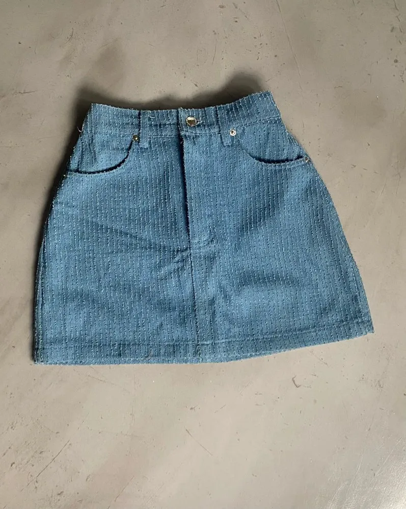 Pollera denim con textura de costura. Estilo acanalada. Elástico en la parte de atrás + boton y cierre delantero. Es tiro alto. Medidas: cintura alta 29cm [cede hasta 31/32cm] - cadera 38cm - largo 37cm - ancho muslos 48cm