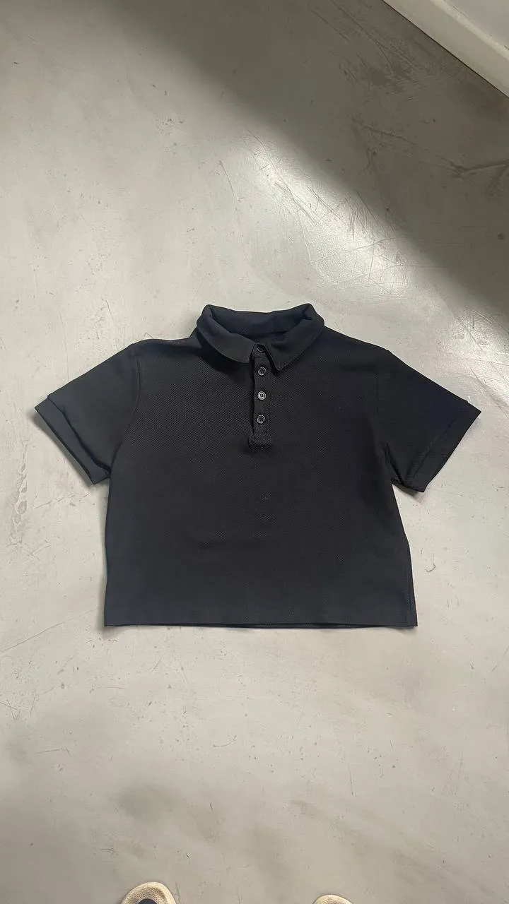 Remera polo negra de manga corta con cuello y botones. Corte crop. Dejo medidas: largo 50cm - axilas 52cm - bicep 23cm - hombros 42cn - largo manga 17cm 