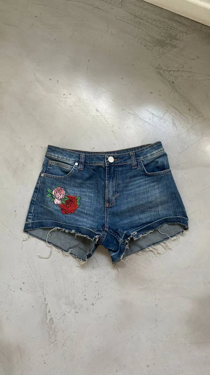 Short de jean con bordado de flores en el frente y un parche circular en el bolsillo trasero. Botón y cierre delantero. Apenas deflecado. Medidas: cintura 38cm - cadera 41cm - largo 28cm - entrepierna 17cm - muslos 30cm. TALLE 42