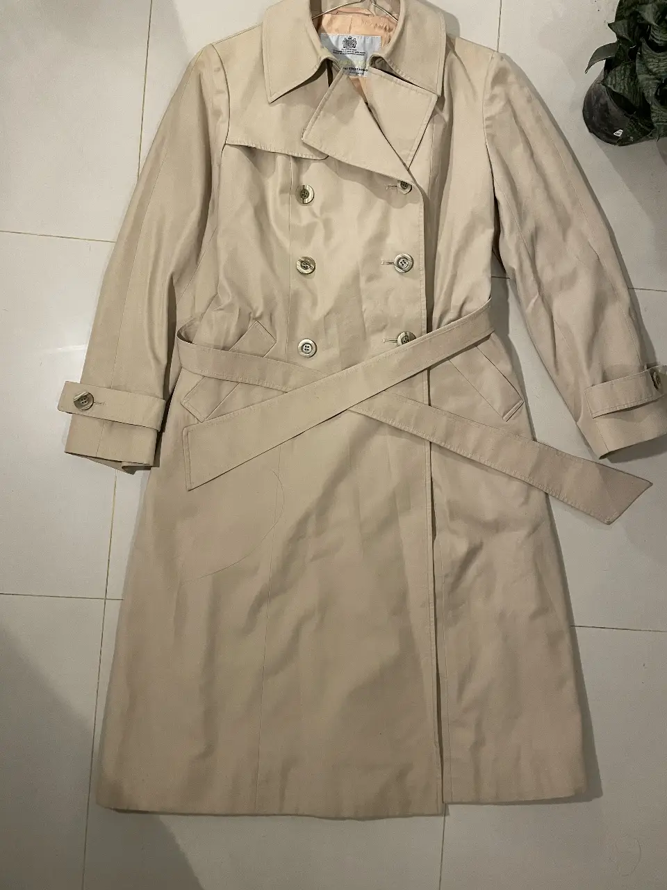 Trench coat clásico en color crudo, ideal para un look elegante y atemporal. Confeccionado en gabardina, este trench cuenta con doble botonadura, cinturón para ajustar la cintura y detalles como solapas y bolsillos. Perfecto para usar en otoño e invierno.