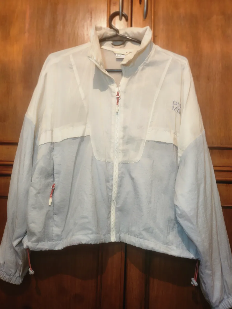 Campera deportiva blanca y gris con cierre al frente. Tiene puños elastizados y cordón ajustable en la cintura.