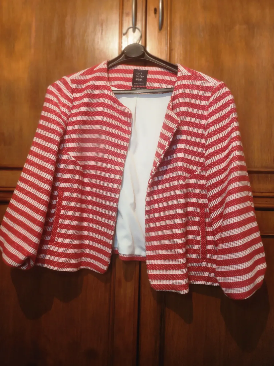 Blazer a rayas rojas y blancas, con cuello redondo y mangas 3/4. Posee dos bolsillos frontales.