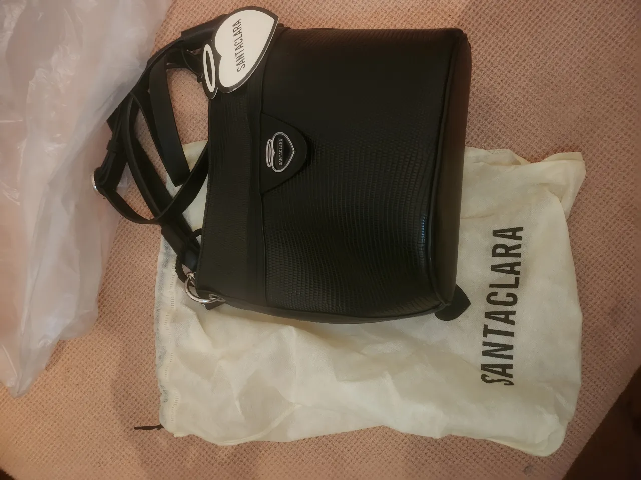 Bolso negro de cuero texturizado con correa ajustable y detalles metálicos. Incluye bolsa de tela para guardarlo.