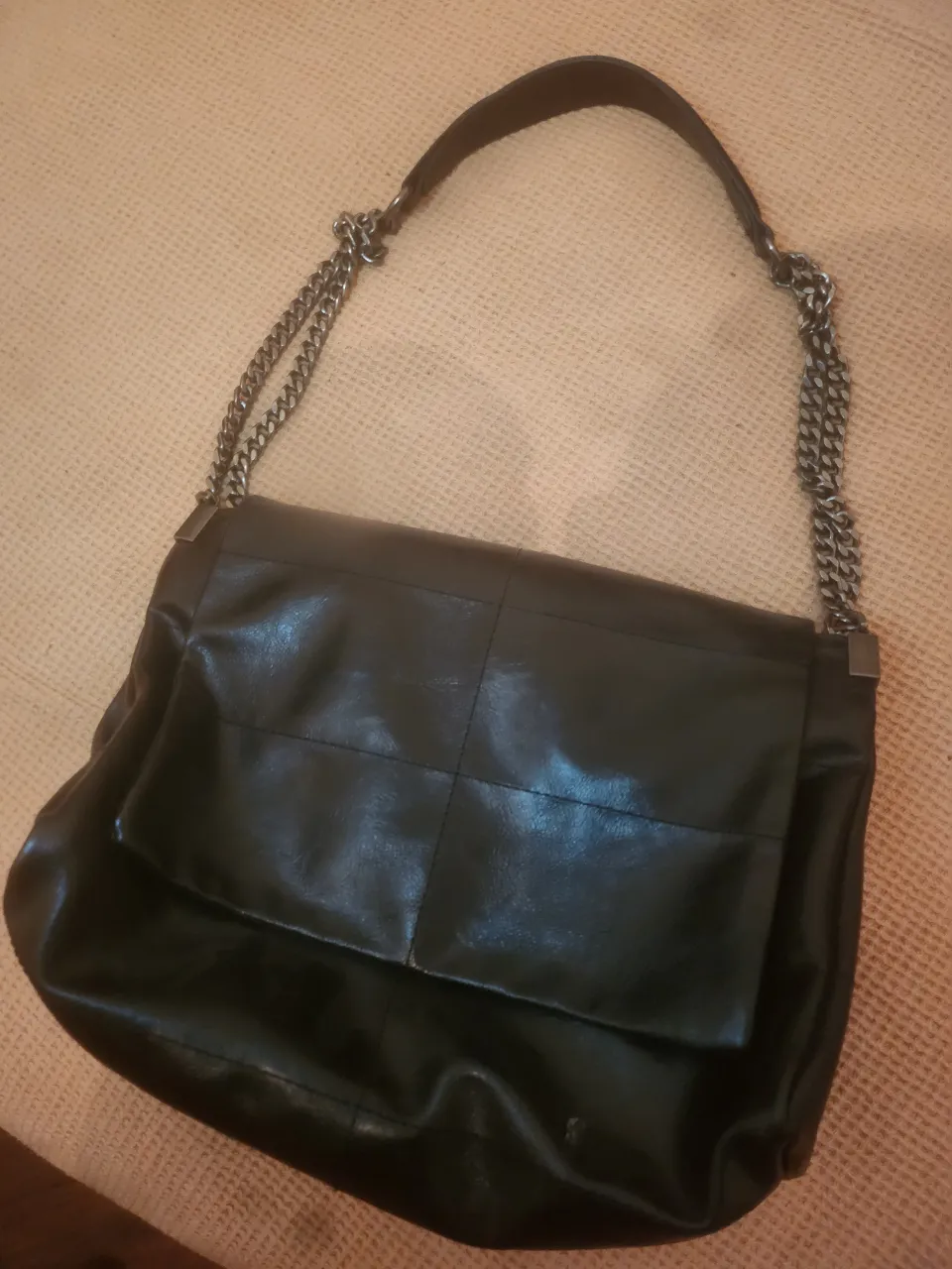Bolso negro de cuero con solapa y correa de cadena.