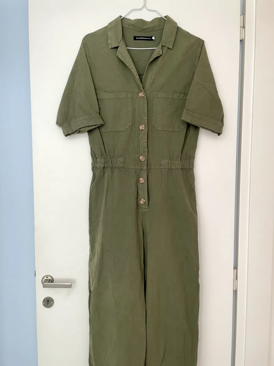 Mono color verde militar. Tiene cuello camisero, mangas cortas, cintura elastizada y botones al frente. En la parte de atrás se soltó la costura pero es de fácil arreglo. 