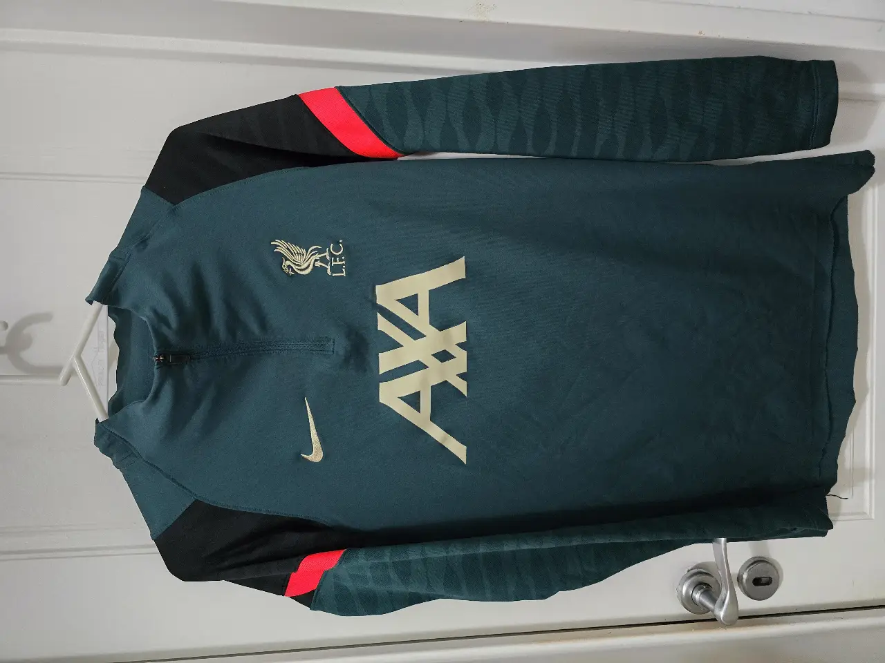 Buzo deportivo de hombre del Liverpool, color verde oscuro con detalles en rojo y negro. Con el logo de Nike y el escudo del equipo. Ideal para entrenar o para uso casual.