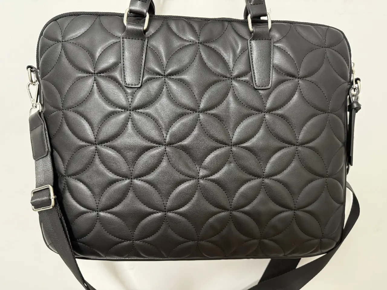 Bolso maletín negro con diseño acolchado. Ideal para llevar tus pertenencias con estilo y elegancia. Cuenta con manijas superiores y correa ajustable para llevar al hombro. Perfecto para el trabajo o cualquier ocasión.