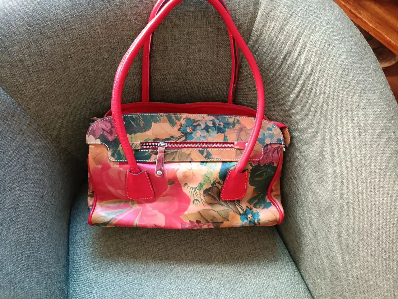 Cartera de mano con estampado floral y detalles en rojo. Ideal para un look casual y femenino.