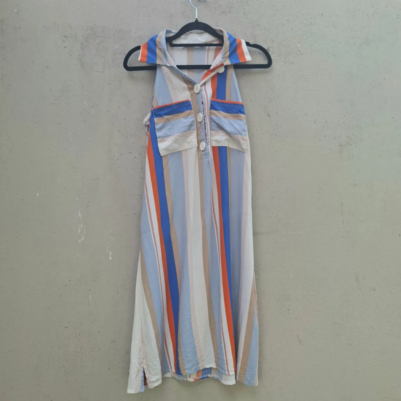 Vestido sin mangas a rayas verticales multicolor con cuello camisero y botones al frente. Posee dos bolsillos superiores con solapa.
