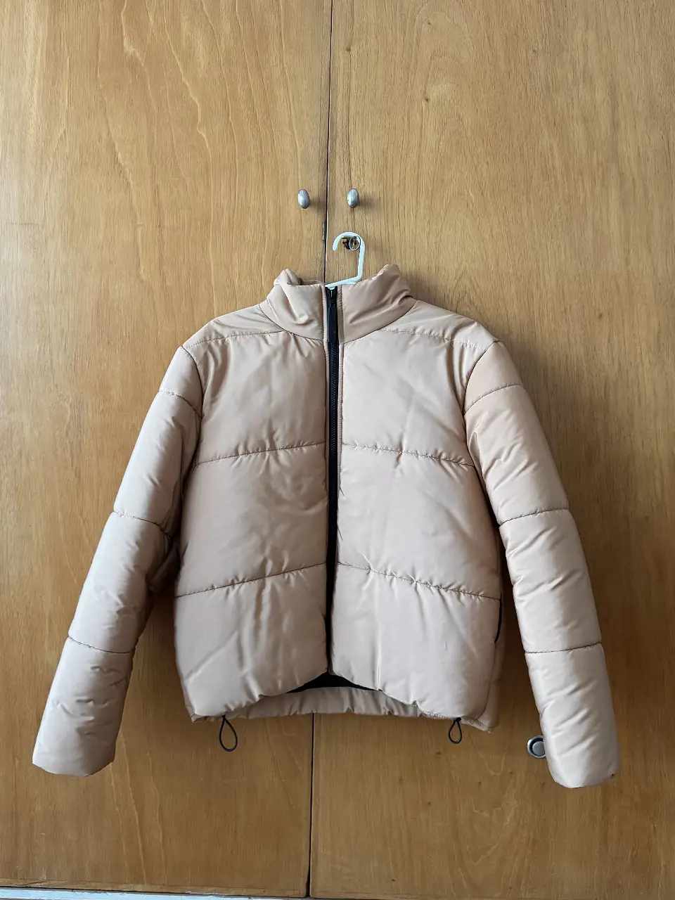 Campera puffer color mostaza, con cierre negro y cuello alto. Tiene elásticos en los lateral para ajustar.
