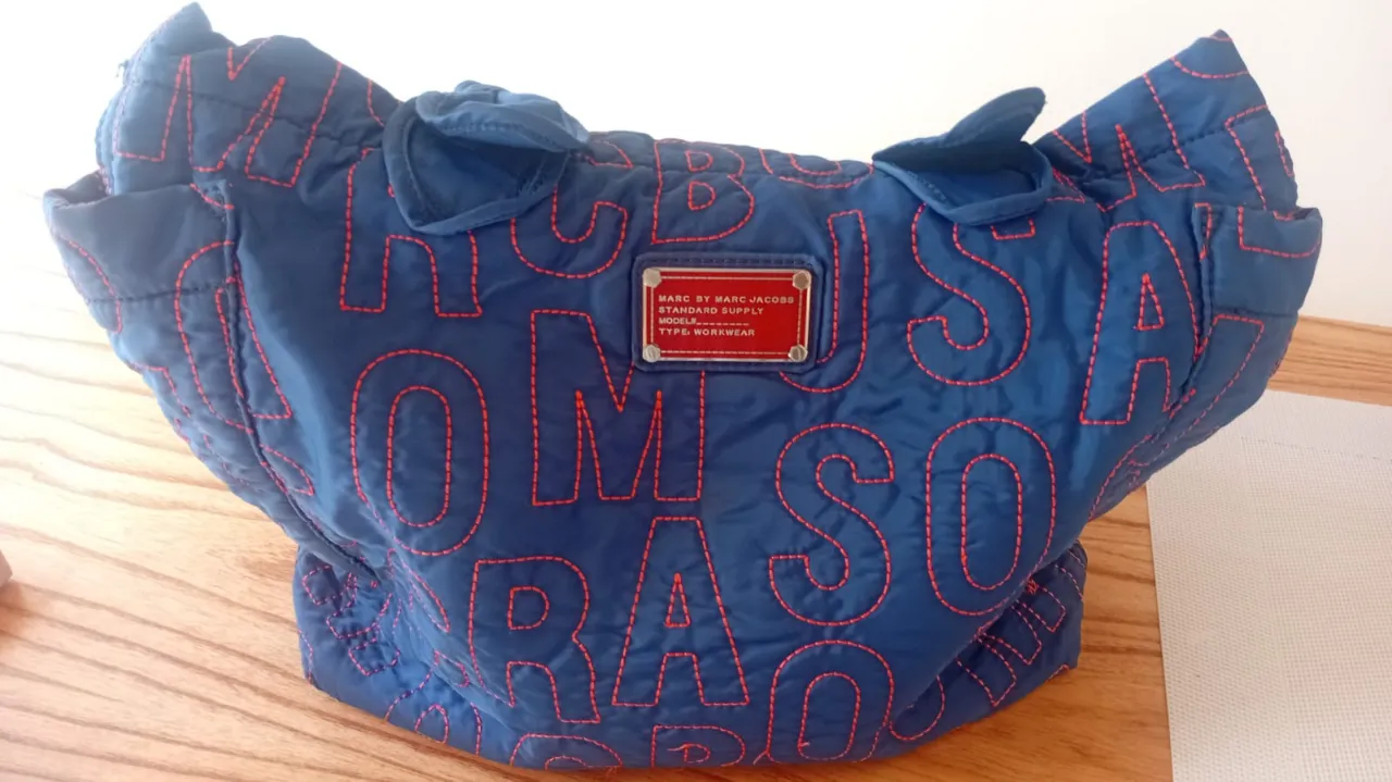 Bolso tote azul marino de Marc Jacobs, con logo de la marca en relieve y costuras en naranja. Ideal para el día a día, para llevar todo lo que necesitás con mucho estilo.ORIGINAL 